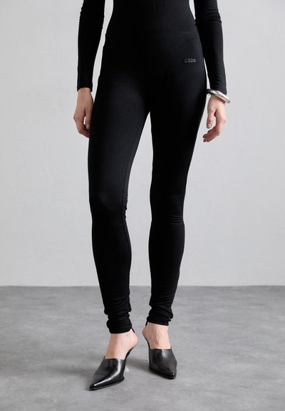Zwarte leggings van rekbare stof, met een gladde textuur en een hoge taille. Gecombineerd met puntige zwarte muilen.