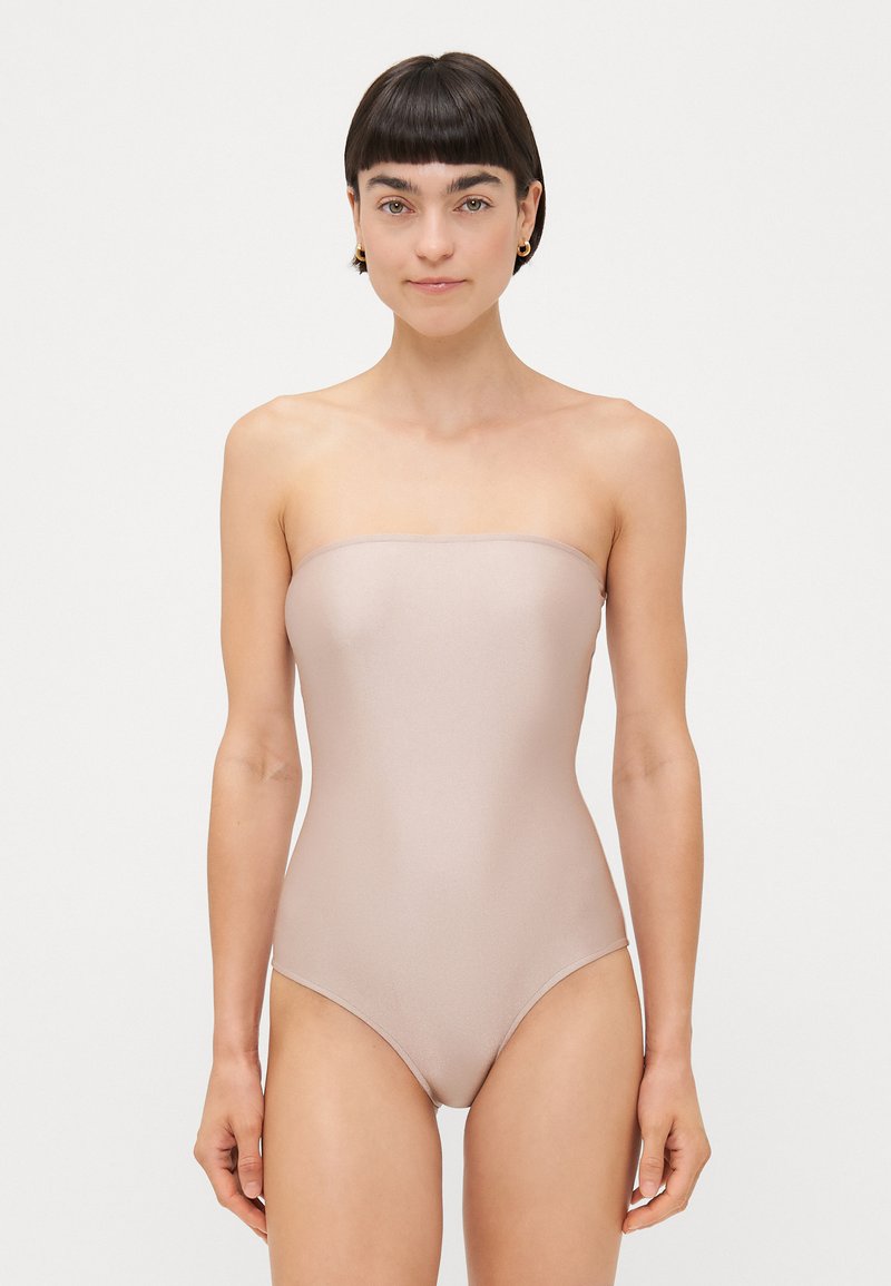 Costum de baie întreg, fără bretele, de culoare nud, cu o textură netedă și lucioasă și un design ajustat, având o siluetă simplă și fără cusături.