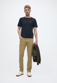 T-shirt col rond marine, pantalon beige, sweat à capuche vert olive, baskets blanches avec des accents camel. Tissu lisse, coupe décontractée, design minimaliste.