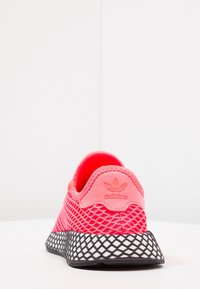 Rosa nätstrumpa med vadderad krage och svart gummisula. Anmärkningsvärda funktioner inkluderar ett diamantmönster på sulan och präglad logotyp.