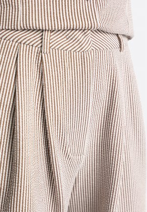 Nahaufnahme von beigefarbenen und braunen, vertikal gestreiften, plisseeartigen Hosen mit Gürtelschlaufen und passendem Bund.