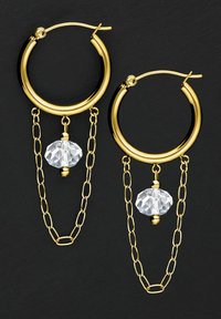 Goldene Creolen mit einem transparenten, facettierten Perlenanhänger, verbunden durch ein Kettenglied-Design, auf einem dunklen Hintergrund.