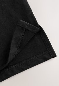 Primo piano di tessuto nero piegato che mostra cuciture dettagliate sui bordi su uno sfondo chiaro.