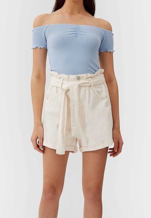 Kvinde iført en lyseblå off-shoulder ribbet top og højtaljede cremede paperbag-shorts med bindebælte.