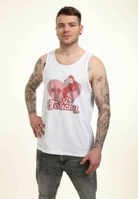 Top sin mangas blanco con un diseño gráfico de una cabra dentro de un corazón rosa, con el texto "No Touchy" en rojo. Acentuado con tatuajes en los brazos.