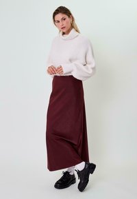 Per didelę baltą megztinį su raukiniu, derinamą su ilga bordo sijonu. Juodi šnuoruojami batai ir balti kojinaičiai užbaigia aprangą.