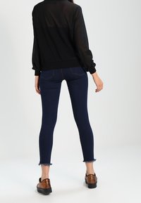 Maglia nera trasparente con maniche a palloncino, abbinata a jeans skinny blu scuro con orli sfrangiati e scarpe platform marroni.
