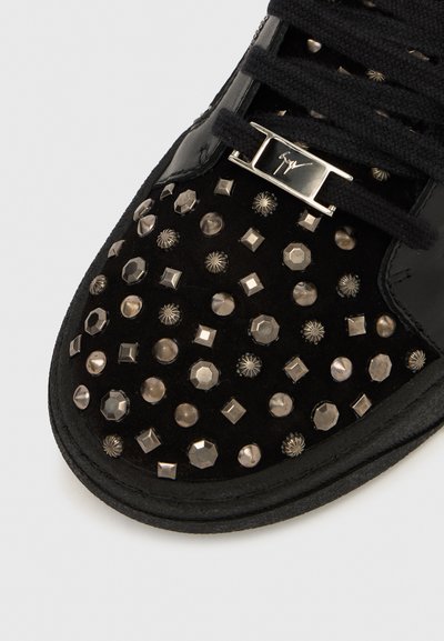 Mustad tossu, millel on tekstureeritud seemisnahast pealiskate, mis on kaunistatud metallist naastudega erinevates kujudes ja suurustes ning mustad paelad.