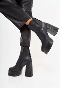 Black leather ankle boots with a chunky high heel, side zipper, and textured detailing on the heel. Smooth finish, modern design.