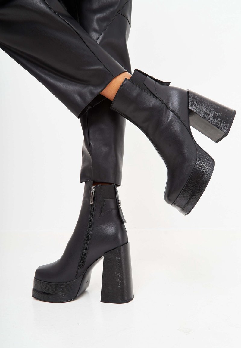 Black leather ankle boots with a chunky high heel, side zipper, and textured detailing on the heel. Smooth finish, modern design.