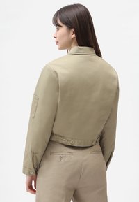 Khaki lühi jakk krae, nupulistumine taga ja küljetasku. Sile tekstuur, puhke disain.