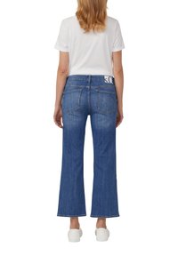 Brede blauwe denim jeans met een hoge taille, voorzien van een witte logo-detail op de achterkant, en gestyled met een plain witte t-shirt en witte schoenen.