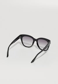 Óculos de sol de plástico preto com um design de olho de gato, lentes em degradê e hastes elegantes. Possui uma marcação subtil de marca na lateral.