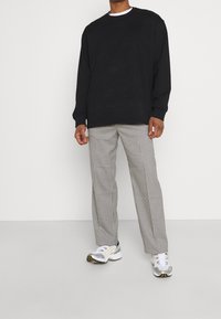Sweat-shirt noir surdimensionné, pantalon à carreaux à motifs, et baskets gris-blanc avec des accents jaunes. Tissu lisse, coupe décontractée.