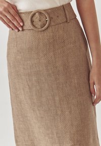 Brązowa lniana spódnica z szerokim paskiem z okrągłą klamrą i teksturowaną powierzchnią. Tkanina ma naturalny, lekko szorstki wygląd.