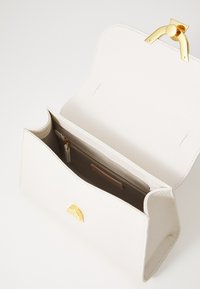 White textured leather handbag with a gold clasp, featuring a spacious interior and a zippered pocket for organization.