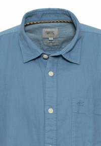 Lyseblå skjorte i en blanding af hør med knap-ned krave, frontplade med knapper og en brystlomme med diskret logo-broderi.