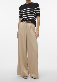 Granatowo-kremowa prążkowana dzianinowa bluzka zestawiona z beżowymi spodniami z wysokim stanem i szerokimi nogawkami, ozdobiona brązowym paskiem. Gładkie tekstury, luźny krój.