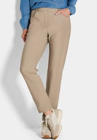 Beige broek gemaakt van zachte stof met een rechte pasvorm, met voorzakken en een gladde textuur, gecombineerd met lichte sneakers.