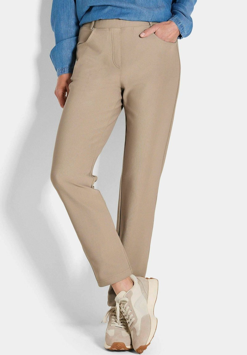 Beige broek gemaakt van zachte stof met een rechte pasvorm, met voorzakken en een gladde textuur, gecombineerd met lichte sneakers.