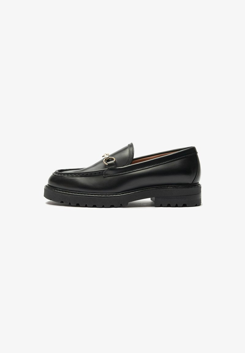 Mocassin noir en cuir avec détail mors métallique, semelle épaisse à crampons et bout moc cousu, présenté de côté sur fond blanc.