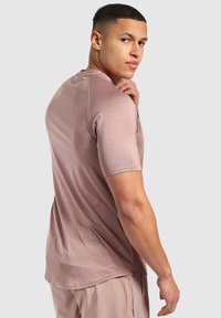 Camisa ajustada de manga corta en color malva claro con una tela texturada, escote redondo y un patrón sutil, llevada por una persona que mira hacia atrás.