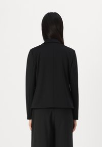 Blazer nero su misura con colletto a punta, maniche lunghe e taglio dritto. Il tessuto liscio e le linee pulite creano un design minimalista.
