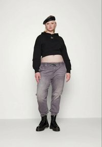 Fekete, rövidített kapucnis pulóver, szürke, szűkített farmernadrág és fekete katonai bakancs. A modellen fekete baret van. Az összeállítás laza szabású és rugalmas derékrésszel rendelkezik.