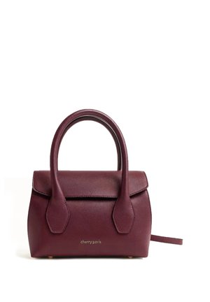 Sac à main en cuir bordeaux avec deux poignées, fermeture à rabat et logo "cherry paris" sur le devant, posé sur un fond blanc.