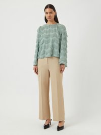 Un top verde menta con texture e strati di frange ondulate, abbinato a pantaloni beige a gamba larga e tacchi in vernice neri.