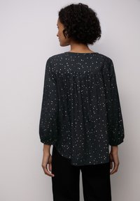 Blusa nera con motivo a pois bianchi, con yoke arricciato e maniche lunghe a palloncino. Tessuto morbido con una vestibilità comoda e orlo arrotondato.