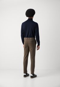 Marineblå turtleneck genser, slim-fit brune bukser og svarte joggesko med hvite detaljer. Glatt stoff, skreddersydd design og minimal detaljer.