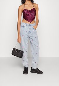Rosa mönstrad crop-top med hjärtformad halsringning, i kombination med ljusblåa jeans i denim med broderade logotyper och svarta sneakers.