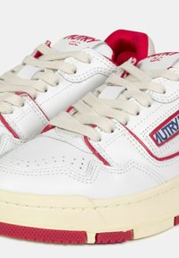 Sneakers in pelle bianca con accenti rossi, suole testurizzate e lacci beige. Il nome del marchio "AUTRY" è visibile sul lato in blu.