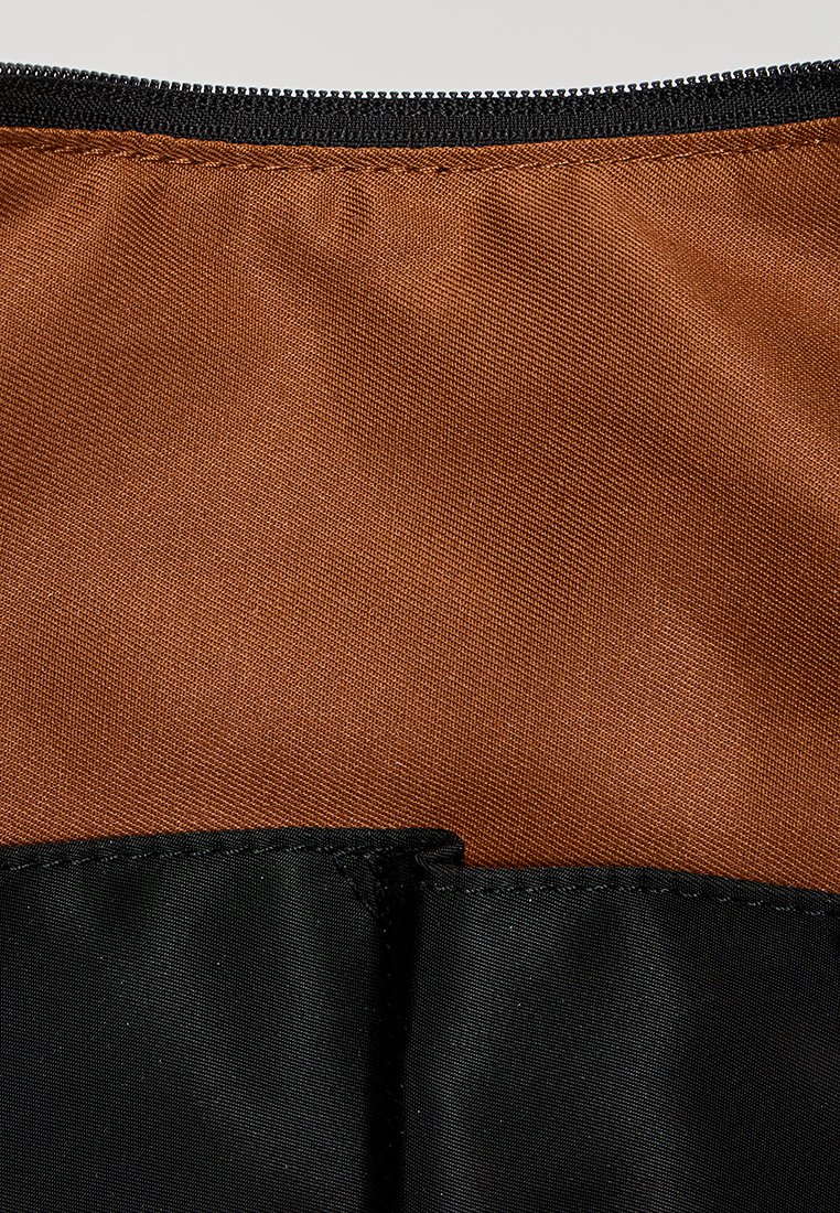 Zbliżenie na brązowy i czarny materiał z detalicznym szyciem wzdłuż szwu, ukazujące strukturę i splot tkaniny.