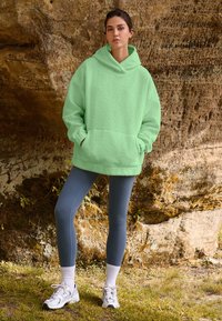 Light green fleece oversized hoodie with a kangaroo pocket, worn over dark blue leggings, paired with white crew socks and white sneakers.