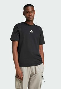 Svart bomullströja med korta ärmar, med en vit triangel-logotyp på bröstet, tillsammans med ljusbeige cargoshorts.