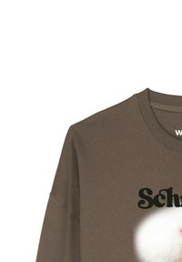 Bruin T-shirt met ronde hals en een close-up afbeelding van het gezicht van een witte kat en een gedeelte van zwarte tekst boven de kat.