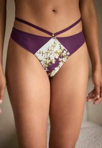 Bikini apakša ar violeta vienkrāsainu audumu un ziedu rakstu detaļu, ar šaurām siksnām un apļveida detaļu priekšpusē.