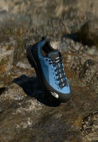 Blue and black hiking shoe with a sleek design, textured upper, laces, and a contrasting black sole. Features lacing system and logo accents.