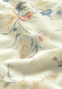 Blumendruckstoff in Creme mit weicher Textur; zeigt mehrfarbige Muster von gelben, blauen und rosa Blumen auf einem leichten Material.