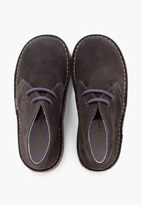 Zapatos de ante marrón oscuro con puntera redonda, que cuentan con dos ojales y cierre de cordones; con costuras decorativas alrededor de la suela y el forro interior.