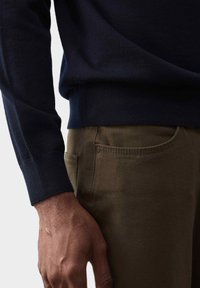 Granatowy sweter dzianinowy z prążkowanym okrągłym dekoltem i mankietami, w połączeniu z oliwkowymi spodniami z bocznymi kieszeniami i detalem w postaci guzika.