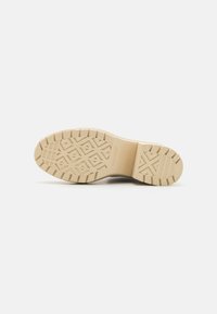 Beige rubber shoe sole with a patterned tread, featuring diamond shapes and horizontal grooves for traction. Smooth upper edge.