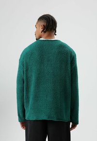 Groene fleece trui met een gestructureerd oppervlak, een losse pasvorm en doorgezakte schouders. De achterkant heeft een afgeronde zoom en minimale details.