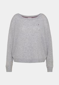 Pull en tricot gris avec un col large, des épaules tombantes et un ourlet côtelé. Il présente un petit logo sur la poitrine gauche. Texture douce.