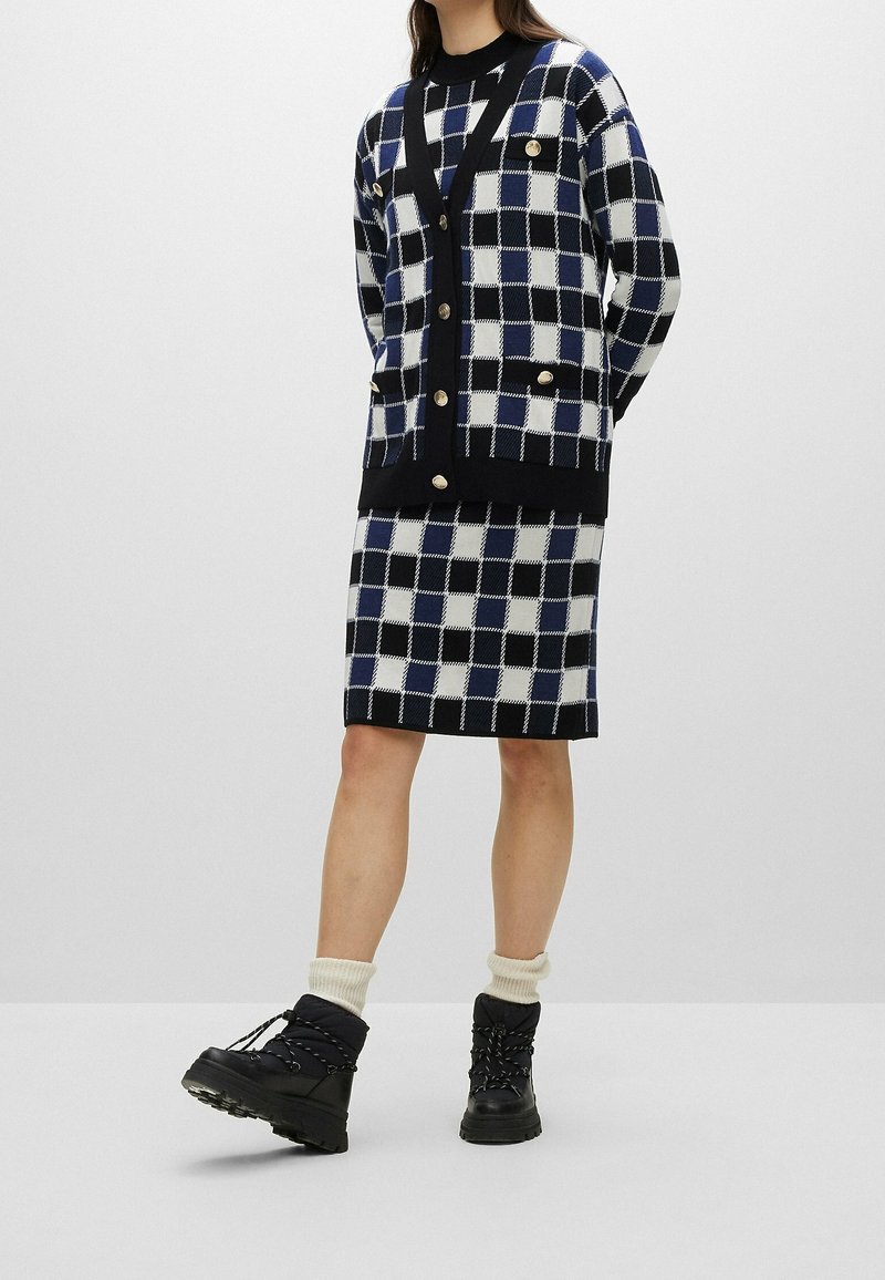 Marinblå och vit rutigt stickad cardigan med knappar, matchad med en kjol i samma tyg. Svarta vinterstövlar och krämfärgade strumpor fulländar outfiten.