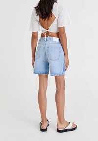 Shorts en denim bleu clair à coupe décontractée, ourlet effiloché et poches arrière, associés à un haut en broderie anglaise blanche avec un détail noué dans le dos.