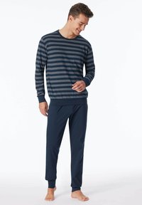 Chemise à rayures bleu marine et gris à manches longues associée à un pantalon bleu marine uni. Tissu doux, coupe décontractée, poignets et ourlets de cheville côtelés. Pieds nus.