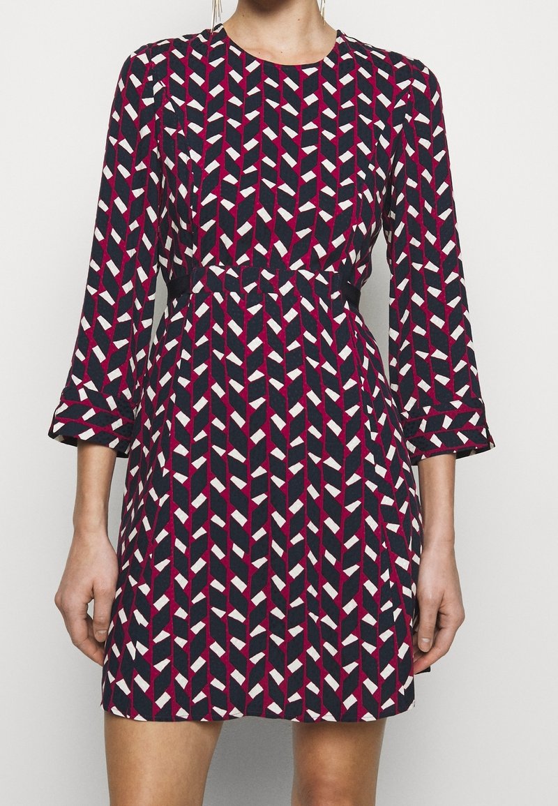 Sukienka z długim rękawem w geometryczny wzór w kolorach granatowym, bordowym i białym. Posiada dopasowaną talię, okrągły dekolt oraz teksturowaną tkaninę o gładkim wykończeniu.